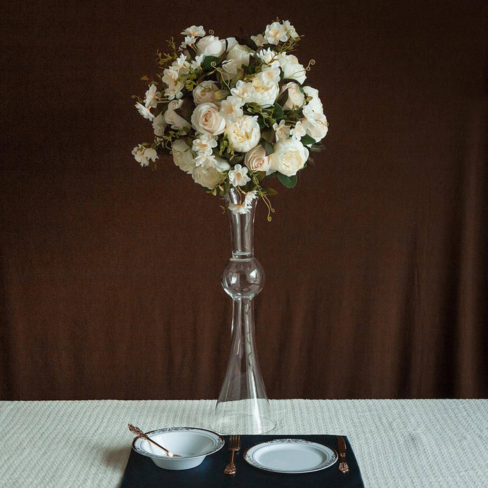 Elegant floral arrangement in a tall glass vase, styled with dinnerware.