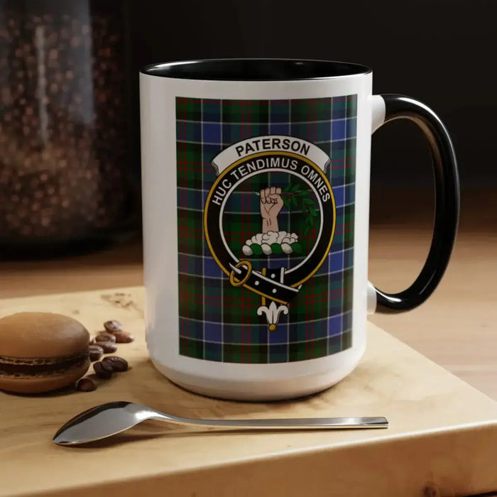 Black-accent Paterson crest mug on a café table beside a macaron and coffee beans.