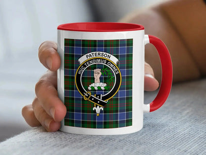 Red-accent Paterson crest mug held in a hand, with a tartan background.
