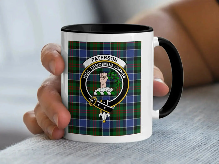 Black-accent Paterson crest mug held in a hand, with a tartan background.