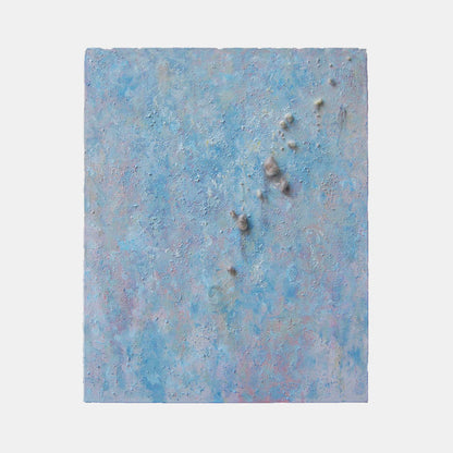The artwork 'Eruption' by Noriko Okada features a textured abstract composition in ethereal light blue and gray tones, with raised elements suggesting volcanic activity. The mixed-media piece combines oil paint and yarn creating a dimensional surface with scattered darker spots emerging from a misty, atmospheric background, measuring 30 x 24 inches.