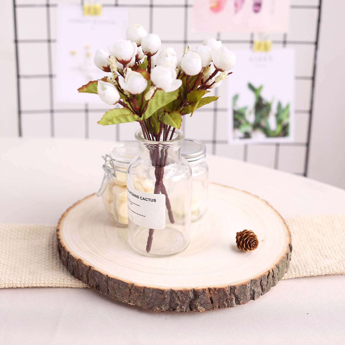 Artificial white flower arrangement in a glass jar on a wooden slice.