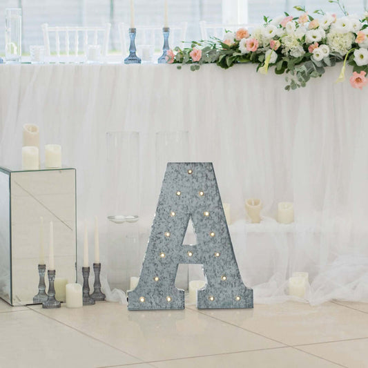 Decorative marquee letter "A" with lights, set against a wedding table backdrop.