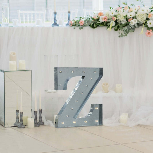 Decorative illuminated letter "Z" in a wedding setting with floral arrangements.